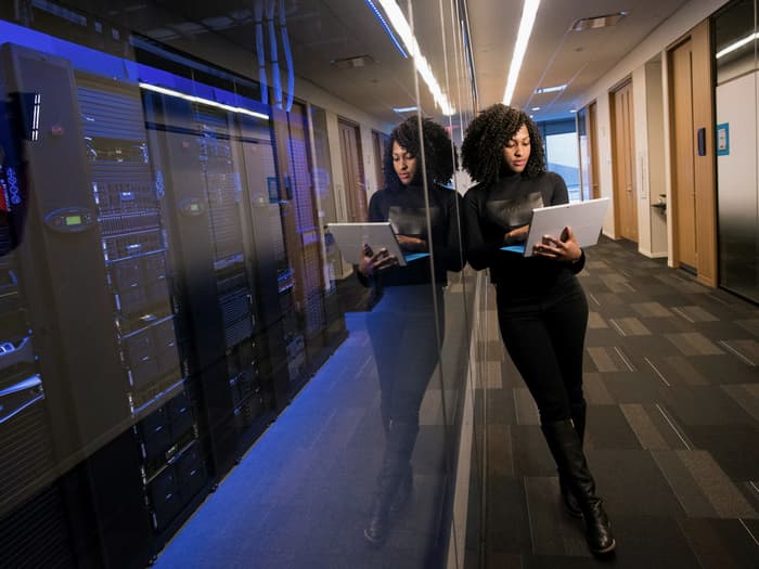 Two engineers walking a data centre aisle with laptops, checking racked equipment