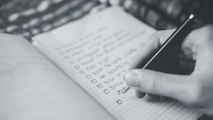 A hand ticking items off a handwritten checklist in a notebook